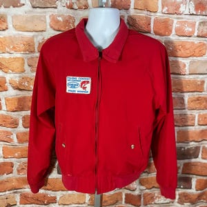 May include: A bright red jacket with a collared neckline and a zipper closure. The jacket features a patch that reads "Fishing Contest Big Fisherman Prize Winner". The jacket has two front pockets and gold-colored buttons.