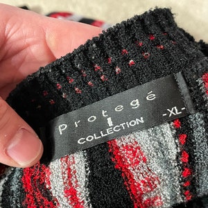 Peut inclure: Pull en maille ray&eacute; noir et rouge avec une &eacute;tiquette noire indiquant "Prot&eacute;g&eacute; Collection -XL-"