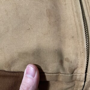 May include: Close-up of a brown canvas jacket with a zipper. The zipper is metal and has a silver finish.
