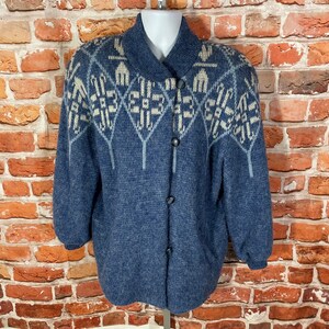 May include: A blue knitted cardigan with a white and gray geometric pattern on the front. The cardigan has a button closure and long sleeves.