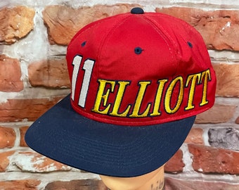 May include: Red and navy blue baseball cap with the number "11" and the name "ELLIOTT" embroidered in yellow.