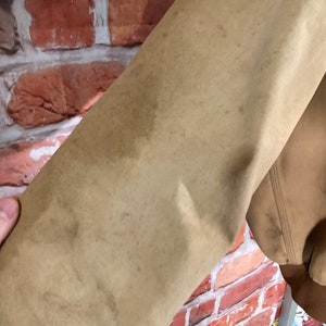 May include: Close-up of the tan-colored sleeve of a jacket. The fabric has a worn look with several brown stains.