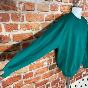 May include: A teal green sweatshirt with long sleeves and a crew neck.