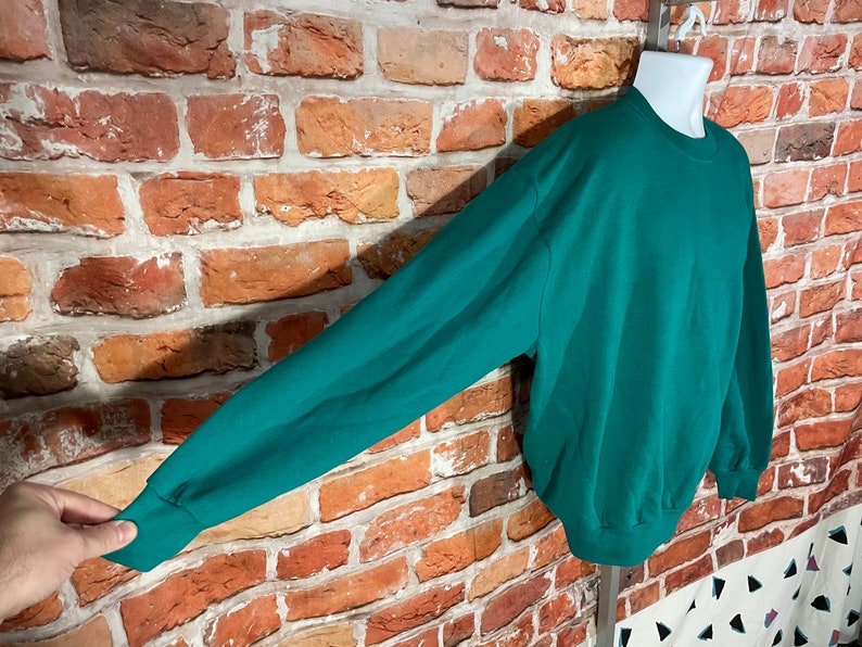 May include: A teal green sweatshirt with long sleeves and a crew neck.