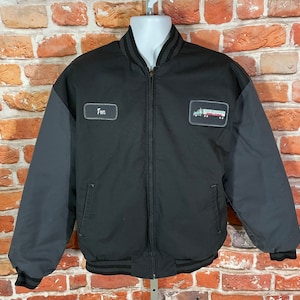 May include: Black bomber jacket with a gray quilted lining. The jacket has a zipper closure and a ribbed collar, cuffs, and waistband. The jacket has a patch on the left chest with the text "Tom" and a patch on the right chest with a truck graphic.