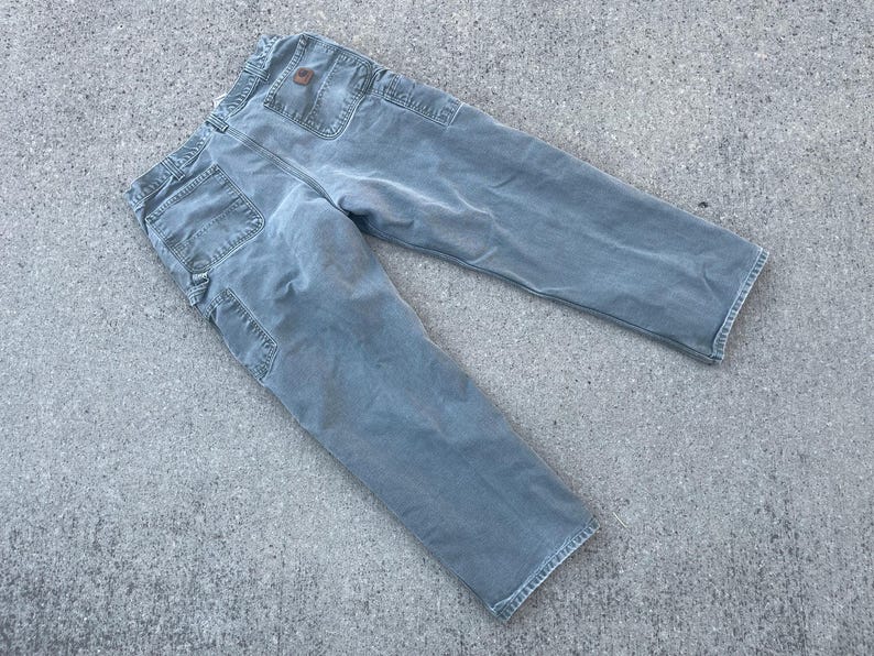 Puede incluir: Un par de pantalones de trabajo de mezclilla azul claro con un parche marr&oacute;n en el bolsillo trasero.