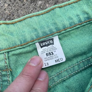 May include: Close-up of a pair of green Levi's 551 jeans. The tag reads "551 Relaxed Fit Tapered Leg" and size 18. The jeans are made of 100% cotton and made in Canada. The stitching is visible.