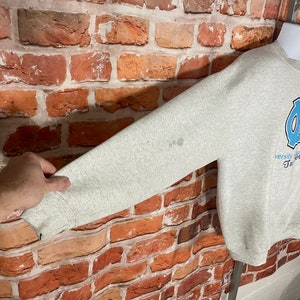 Puede incluir: Sudadera gris con un logotipo azul y blanco de la Universidad de Carolina del Norte Tar Heels y el texto "Varsity Carolina Tar Heels" en la parte delantera.