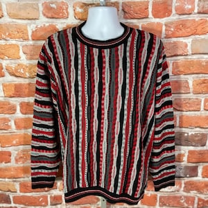 Peut inclure: Un pull ray&eacute; avec un motif noir, rouge et gris. Le pull a un col rond et des manches longues.