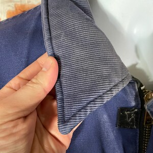May include: Close-up of a navy blue jacket with a zipper closure and a corduroy collar. The collar is folded down and the zipper is partially open.