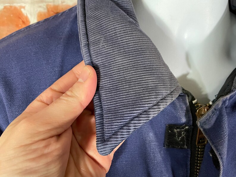 May include: Close-up of a navy blue jacket with a zipper closure and a corduroy collar. The collar is folded down and the zipper is partially open.