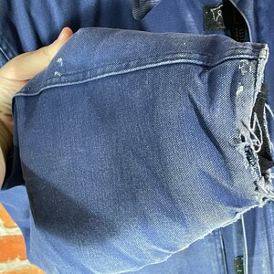 May include: A blue denim work jacket with a frayed cuff. The jacket has a zipper closure and multiple pockets.