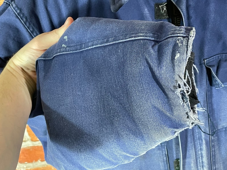 May include: A blue denim work jacket with a frayed cuff. The jacket has a zipper closure and multiple pockets.
