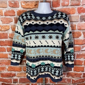 May include: A blue, white, and brown patterned sweater with a crew neck. The sweater has a design of stars, moons, and wavy lines.