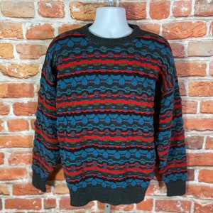 May include: A colorful patterned sweater with a crew neck. The sweater has a geometric design in shades of blue, red, green, and black.