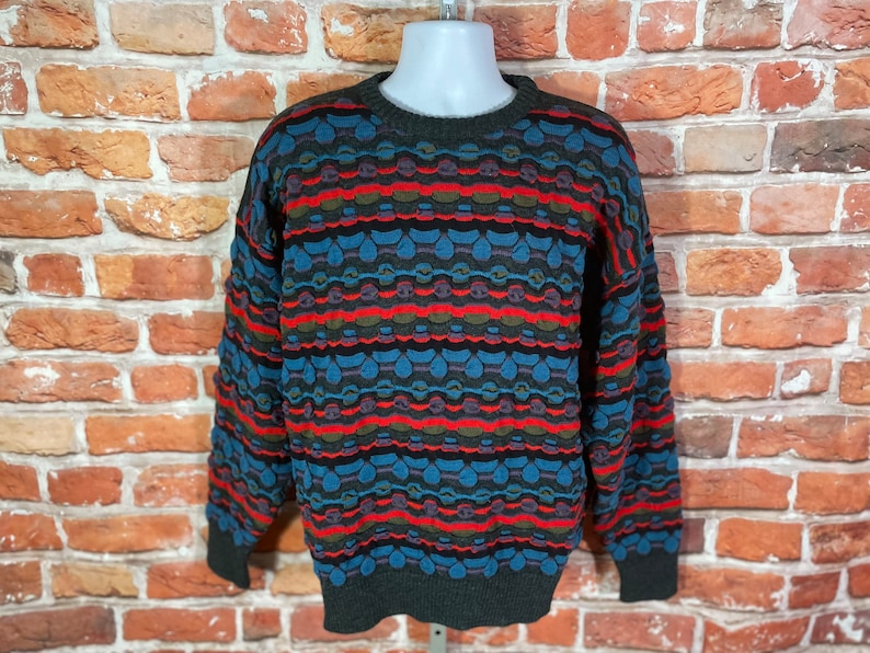 May include: A colorful patterned sweater with a crew neck. The sweater has a geometric design in shades of blue, red, green, and black.