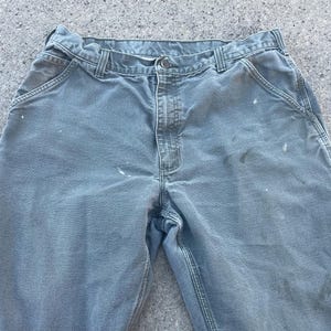 Puede incluir: Un par de pantalones de trabajo verde claro con salpicaduras de pintura blanca. Los pantalones tienen un dise&ntilde;o tradicional de cinco bolsillos y cierre de bot&oacute;n.