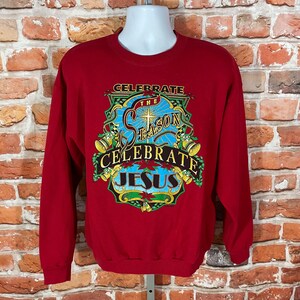 May include: Red Christmas sweatshirt with a colourful graphic design that says "Celebrate the Season Celebrate Jesus".