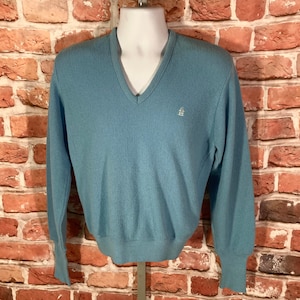 May include: A light blue v-neck sweater with a small embroidered logo on the chest.