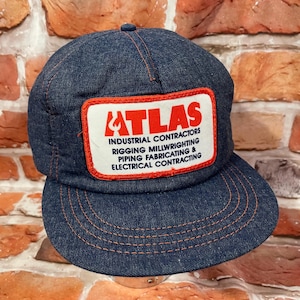 May include: A blue denim trucker hat with a red and white patch that says "ATLAS INDUSTRIAL CONTRACTORS RIGGING MILLWRIGHTING PIPING FABRICATING & ELECTRICAL CONTRACTING".