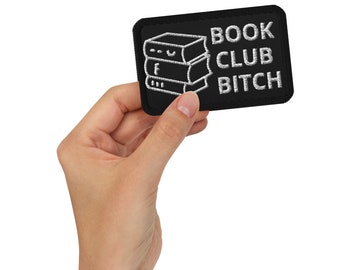 Puede incluir: Parche bordado negro con las palabras "BOOK CLUB BITCH" en blanco, junto con una pila de tres libros. El parche es rectangular con esquinas redondeadas.