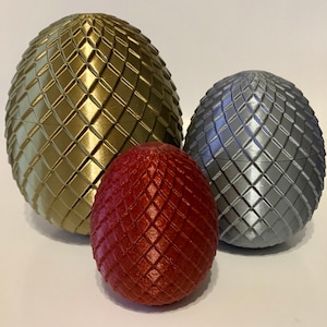 May include: Three dragon eggs, one gold, one silver, and one red. The eggs are made of a textured material and have a detailed design.