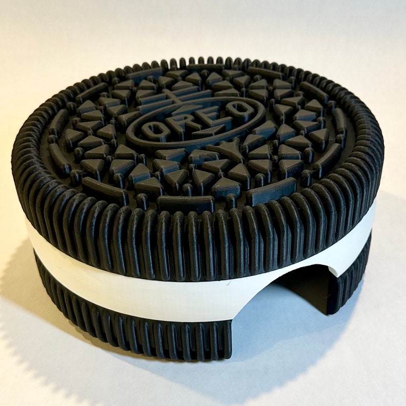 May include: A black and white Oreo cookie-shaped cookie jar with a white interior. The cookie jar has a hole in the side for easy access.