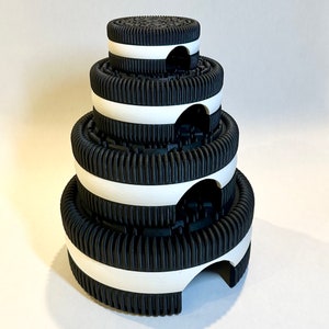 May include: A stack of four black and white Oreo cookie-shaped containers with a white rim around each one. The containers are stacked in a pyramid shape.