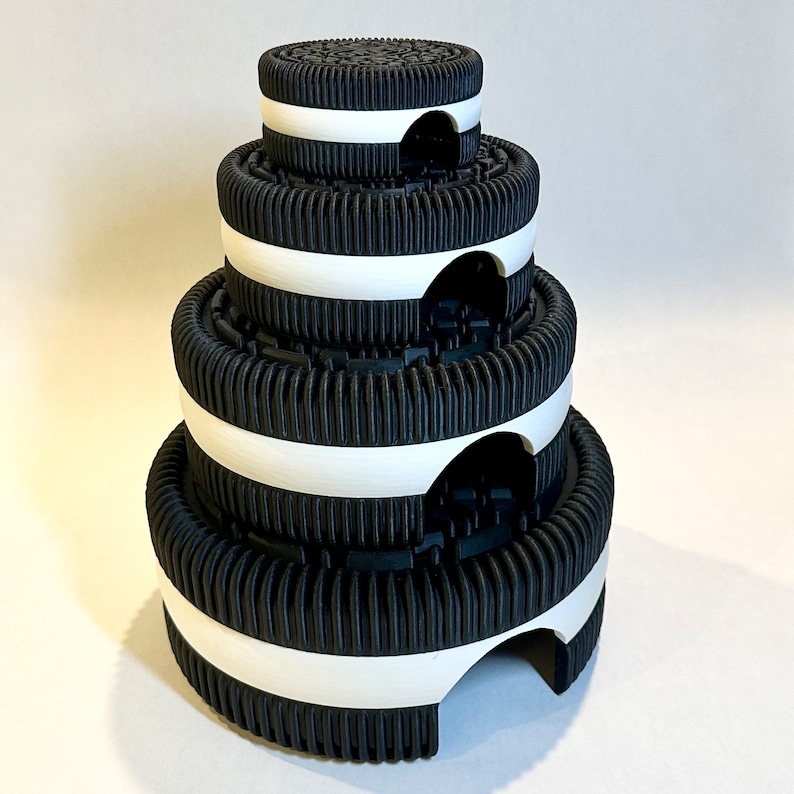 May include: A stack of four black and white Oreo cookie-shaped containers with a white rim around each one. The containers are stacked in a pyramid shape.