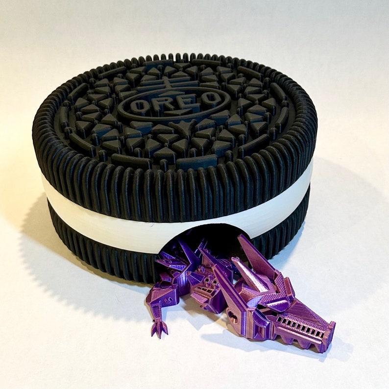 May include: A black and white Oreo cookie with a purple dragon figurine emerging from the center. The dragon is detailed with intricate scales and a textured surface.