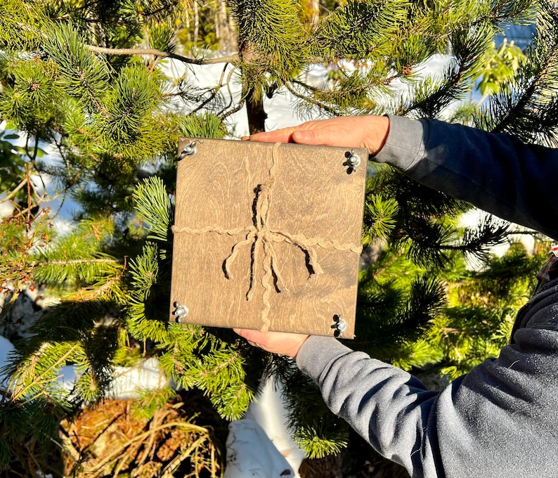 May include: A square wooden box with a rustic brown finish. The box is tied with twine and has metal corner accents.