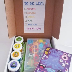May include: A white cardboard box with a to-do list that says "Imagine, Explore, Create, Play, Have Fun! Great Job!" The box contains a set of monster-themed slime, googly eyes, pom-poms, pipe cleaners, and stickers.