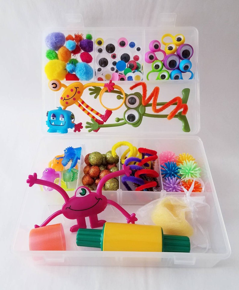 May include: A clear plastic storage box filled with colourful craft supplies for kids. The box contains googly eyes, pom poms, pipe cleaners, and other fun items.