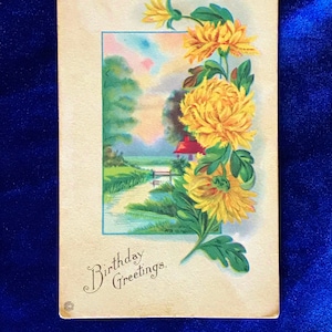 Könnte beinhalten: Vintage-Postkarte mit einer Aquarell-Illustration eines Häuschens an einem Fluss mit einer Brücke. Gelbe Blumen befinden sich im Vordergrund mit dem Text "Birthday Greetings".