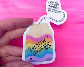 Puede incluir: Una pegatina de una bolsita de té con un diseño de arcoíris y el texto "CREATIVE CONFIDENCE". La bolsita de té tiene una cuerda atada con una etiqueta que dice "STEEP for 5-6 Minutes and ENJOY WITH 60ME ART SUPPLIES".