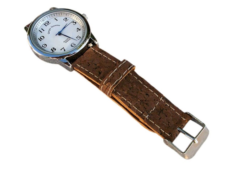 May include: A silver watch with a white face and black numbers. The watch has a brown cork band with white stitching and a silver buckle.