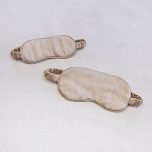 May include: Two beige sleep masks made of soft fabric with elastic straps.
