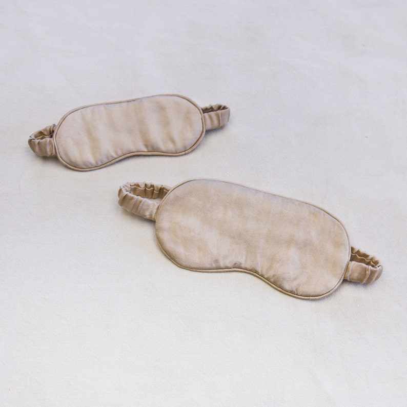 May include: Two beige sleep masks made of soft fabric with elastic straps.