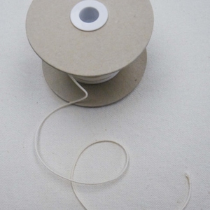 May include: A spool of white elastic cord on a cardboard spool. The cord is wound around the spool and a small amount of cord is unwound.