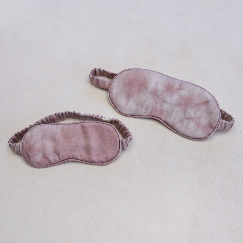 May include: Two pink eye masks made of soft fabric. One mask has a tie-dye pattern and the other is a solid color.