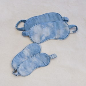 May include: Four blue sleep masks made of soft fabric with a tie-on design. The masks have a tie-dye pattern in shades of light and dark blue.