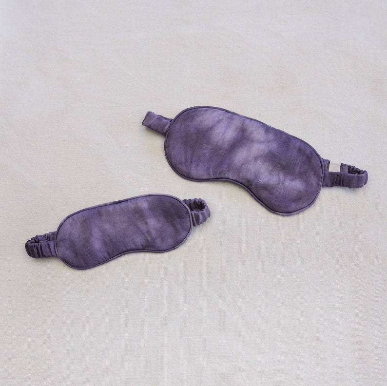May include: Two purple sleep masks made of silk. The masks have a tie-dye pattern.