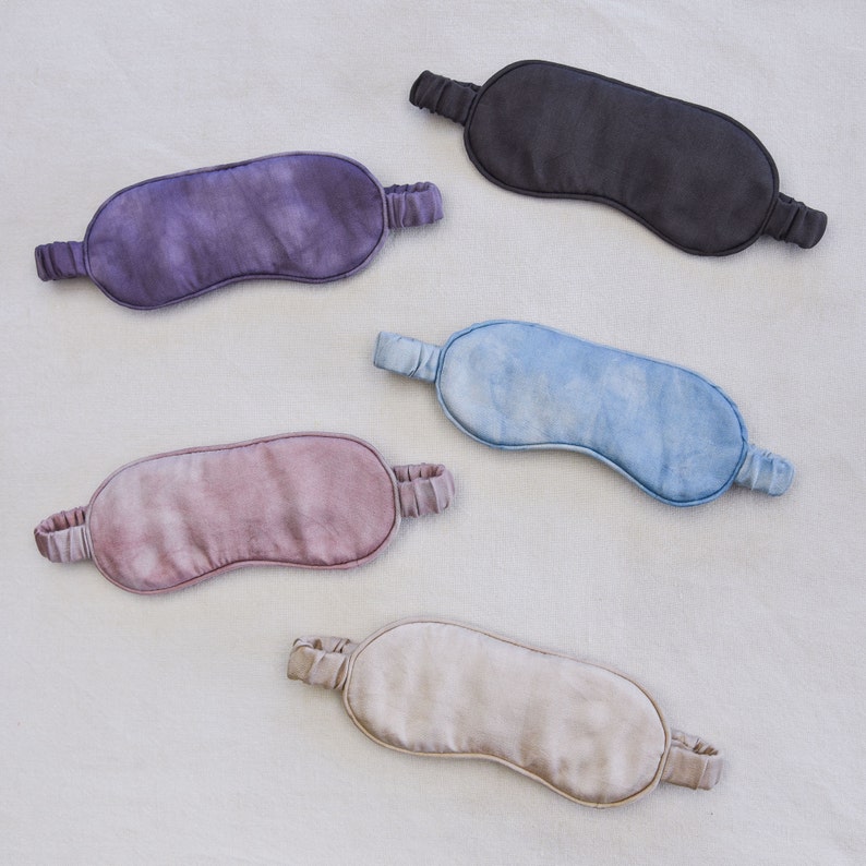 May include: Five silk sleep masks in different colors. The masks are made of soft, smooth silk and have adjustable straps. The colors are purple, blue, pink, beige, and black.