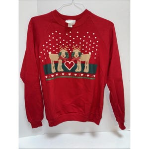 May include: Red Christmas sweatshirt with a festive design. The graphic features two reindeer with green and red scarves, a heart, and white polka dots. The sweatshirt has long sleeves and a crew neck.