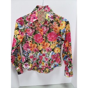 May include: A long-sleeved button-down shirt with a vibrant floral pattern. The shirt features a colorful array of pink, yellow, orange, and blue flowers on a black background. The collar and cuffs are visible, and the shirt is hanging on a hanger.