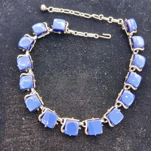 May include: A silver-toned metal link bracelet featuring a series of smooth, square-shaped deep blue cabochons. The bracelet includes a delicate chain extension with a small spherical bead at the end and a hook-style clasp for secure fastening.