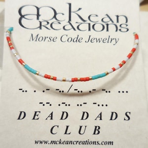 May include: A white card with the text "McKean Creations Morse Code Jewelry" and a bracelet made of white, red, and turquoise beads. The bracelet spells out "DEAD DADS CLUB" in Morse code.