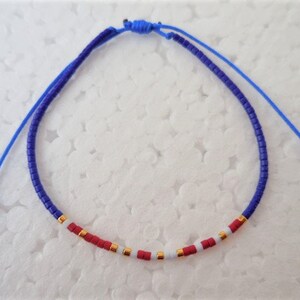 May include: A blue and white beaded bracelet with red accents. The bracelet is made of small beads and has a simple design.