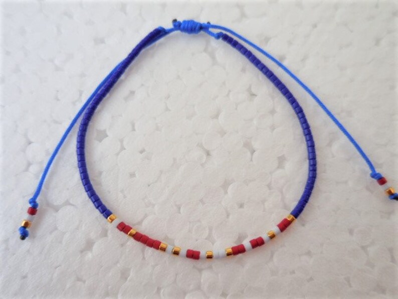May include: A blue and white beaded bracelet with red accents. The bracelet is made of small beads and has a simple design.