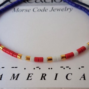 May include: A red, white, and blue beaded bracelet with gold accents. The bracelet spells out "AMERICA" in Morse code.